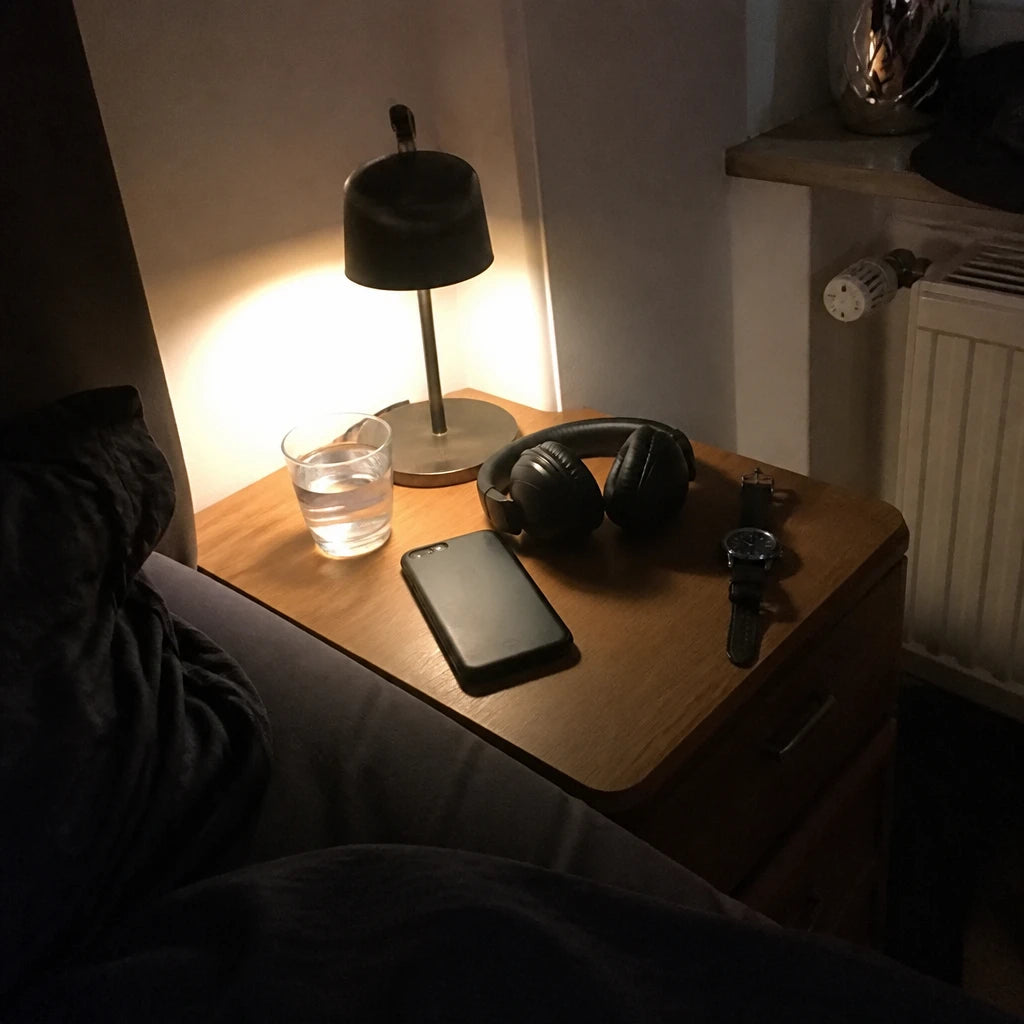 Nachttisch bei Nacht: Handy umgedreht neben Kopfhörern im warmen Lampenlicht